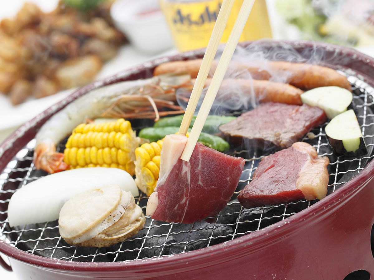 炭火焼肉で使う焼肉網の上で牛肉やウインナー、ホタテ、エビ、トウモロコシ、ナス、玉ねぎが焼かれている様子