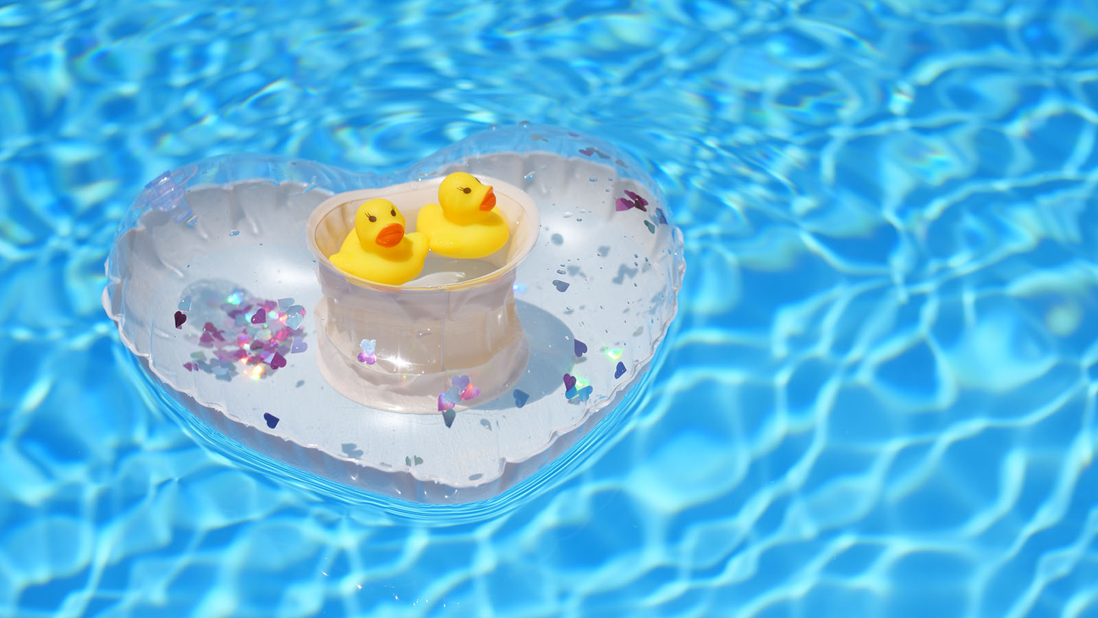 プールに浮かんだハートの浮き輪ドリンクホルダーの中心に黄色いアヒルのおもちゃ2個が入っている