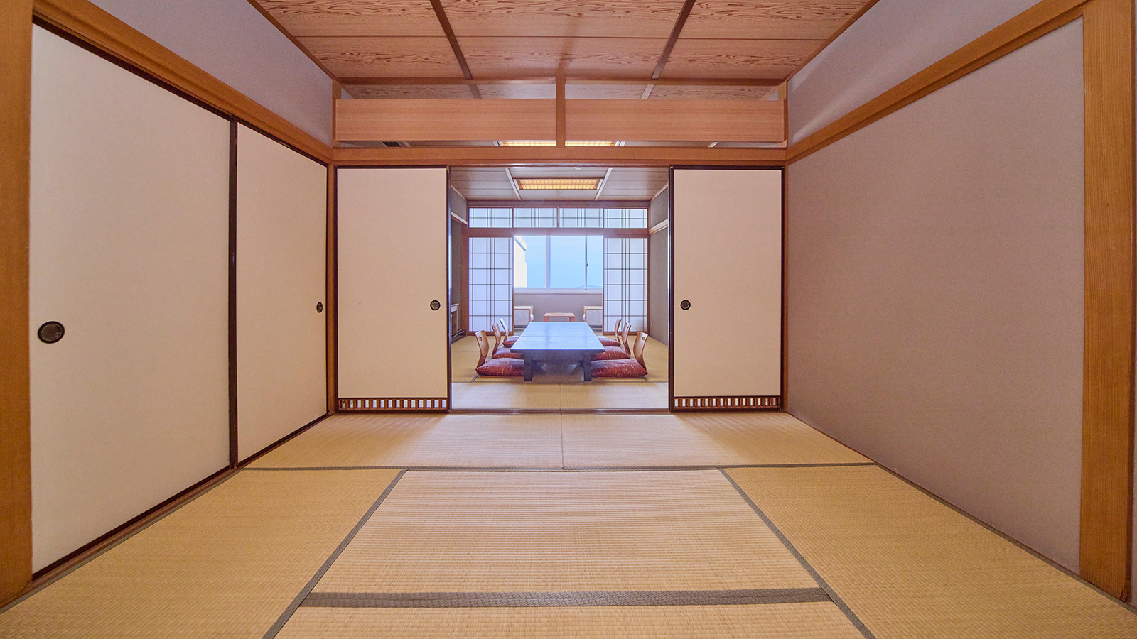 和室18畳・襖で仕切れる二間続きの広い畳の部屋・奥に座椅子と座卓と窓際の椅子が見える