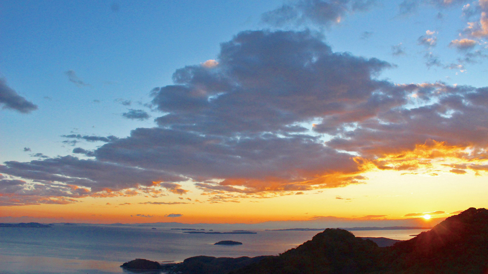 大きな雲が流れる空と夕日とオレンジ色に染まる海